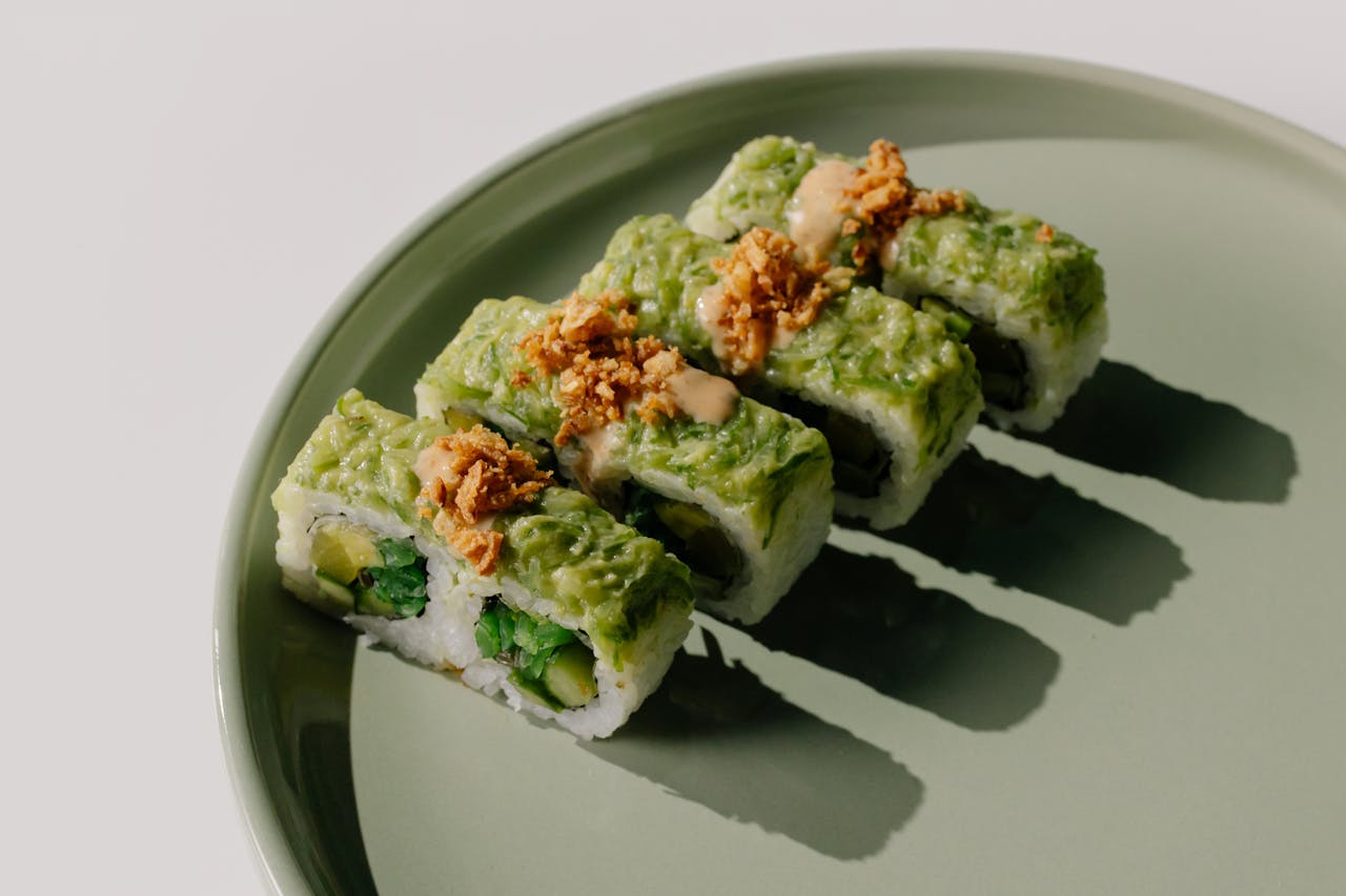 Close-up of vibrant sushi rolls with avocado and crispy topping on a stylish green plate.